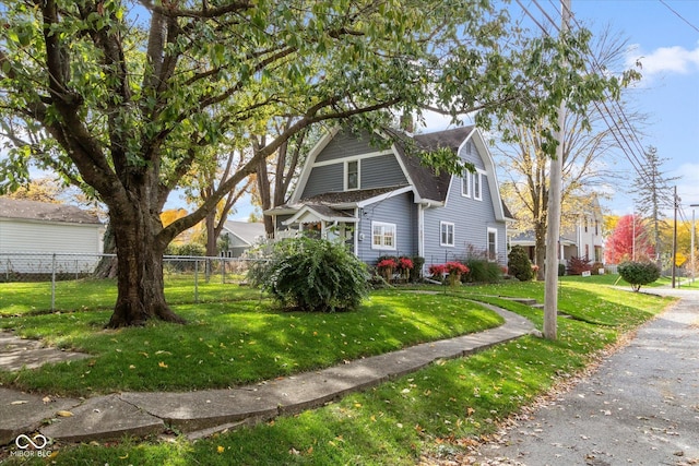 view of front of house with a gambrel roof, a shingled roof, a front lawn, and fence