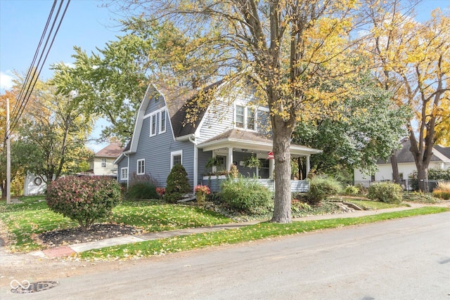 view of front facade with a gambrel roof, a porch, and a front yard