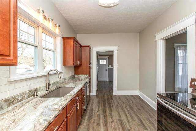 kitchen featuring light stone countertops, baseboards, dark wood finished floors, a sink, and appliances with stainless steel finishes