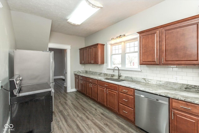 kitchen with tasteful backsplash, dark wood finished floors, light stone counters, stainless steel appliances, and a sink