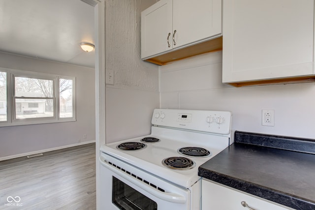 kitchen with white electric range oven, wood finished floors, baseboards, white cabinets, and dark countertops