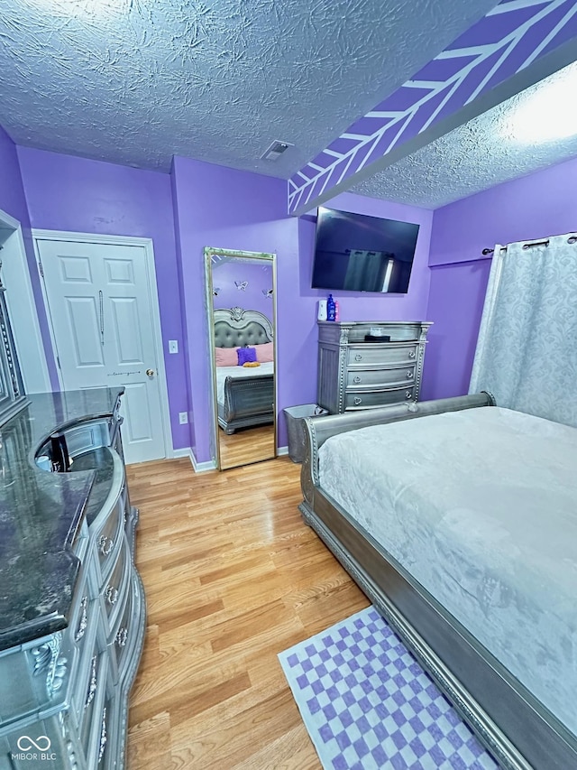 bedroom with baseboards, visible vents, light wood-type flooring, and a textured ceiling