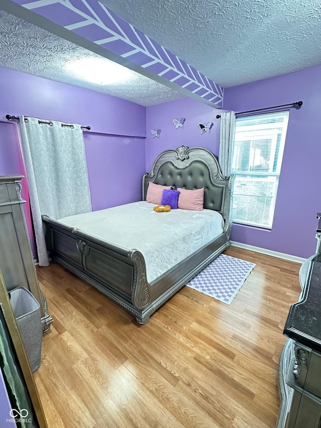 bedroom featuring baseboards, a textured ceiling, and wood finished floors