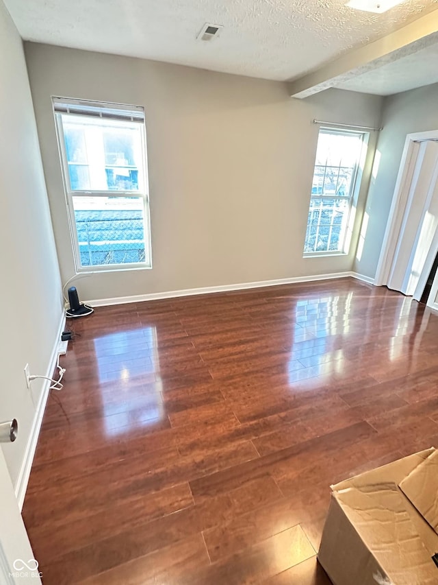 unfurnished room with visible vents, a textured ceiling, baseboards, and wood finished floors