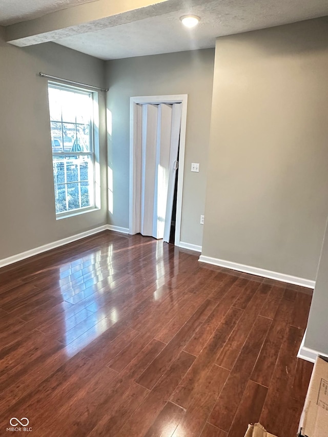 empty room with baseboards, a textured ceiling, and dark wood-style flooring