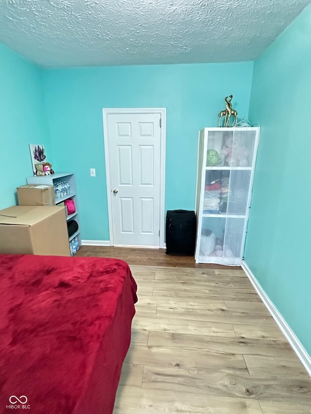 bedroom featuring baseboards, a textured ceiling, and wood finished floors