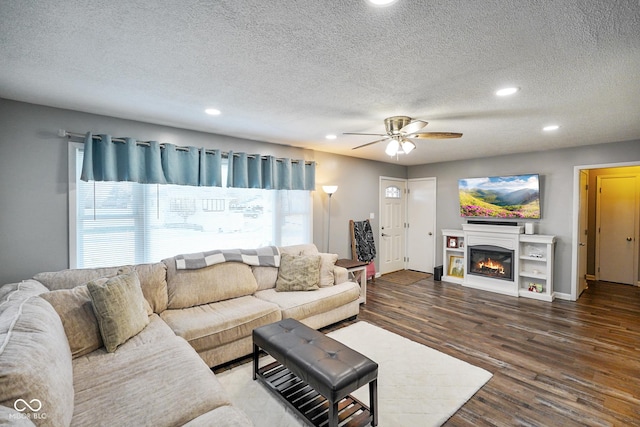 living area with a ceiling fan, a textured ceiling, a glass covered fireplace, wood finished floors, and recessed lighting