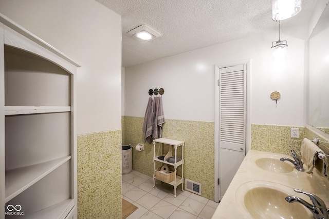 bathroom with visible vents, wainscoting, a textured ceiling, and a sink