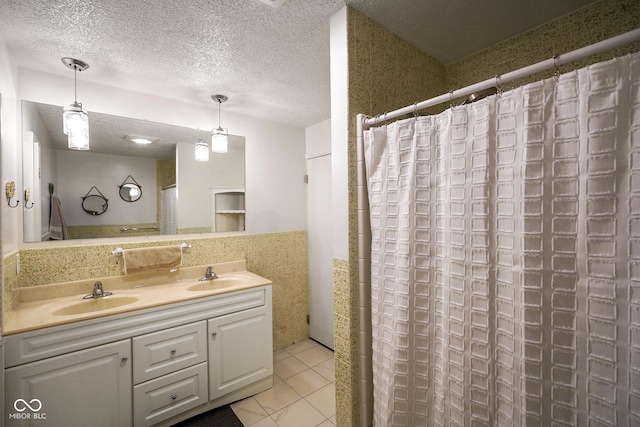 bathroom with a textured ceiling, double vanity, tile patterned flooring, and a sink