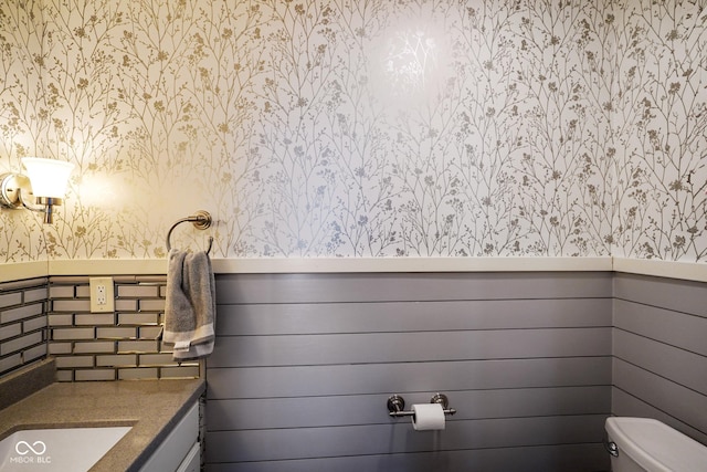 bathroom featuring wallpapered walls, toilet, vanity, and a wainscoted wall