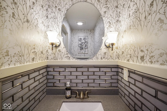 bathroom featuring wainscoting, wallpapered walls, and a sink