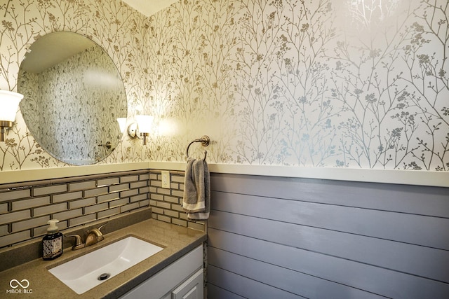 bathroom with wallpapered walls, vanity, and wainscoting