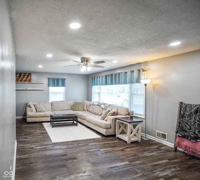 living area with a wealth of natural light, visible vents, a textured ceiling, and wood finished floors