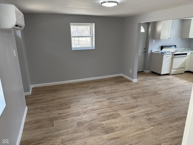 interior space with an AC wall unit, light wood-style flooring, electric stove, light countertops, and baseboards