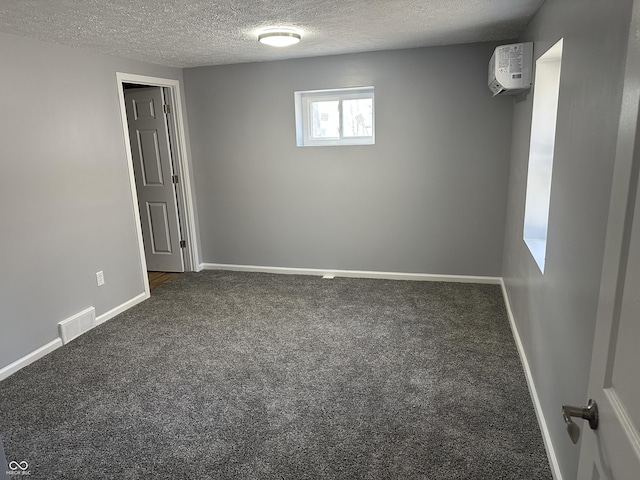 carpeted empty room featuring visible vents, a textured ceiling, an AC wall unit, and baseboards