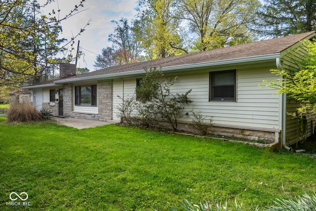 back of house with a patio, a lawn, stone siding, and a chimney