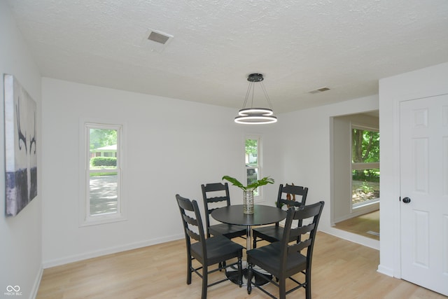 dining space featuring a textured ceiling, light wood-style floors, and a healthy amount of sunlight