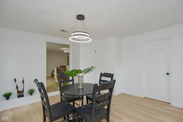 dining room with light wood finished floors, visible vents, and a textured ceiling