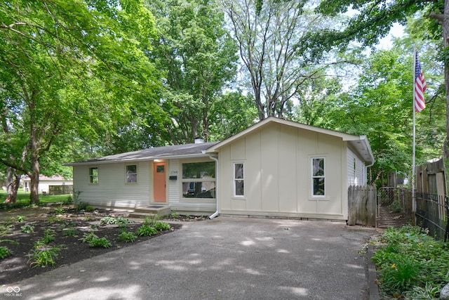 ranch-style home featuring aphalt driveway, board and batten siding, and fence