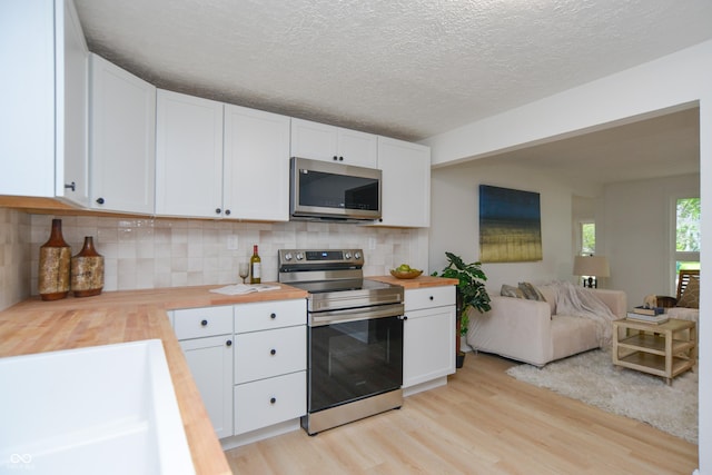 kitchen featuring light wood-type flooring, appliances with stainless steel finishes, open floor plan, and butcher block counters