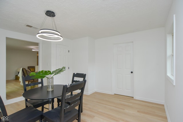 dining room featuring light wood-type flooring, visible vents, baseboards, and a textured ceiling