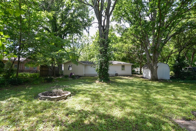 view of yard featuring a storage shed, an outdoor structure, fence, and an outdoor fire pit