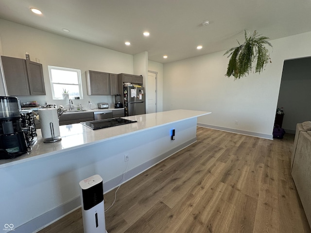 kitchen with a peninsula, wood finished floors, light countertops, and freestanding refrigerator