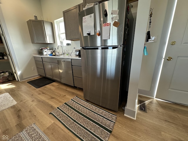 kitchen featuring light wood-type flooring, stainless steel appliances, baseboards, and light countertops