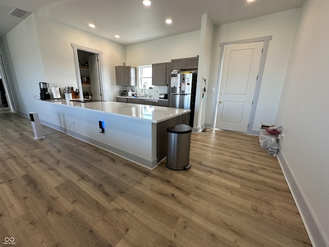 kitchen with recessed lighting, a peninsula, freestanding refrigerator, wood finished floors, and a sink