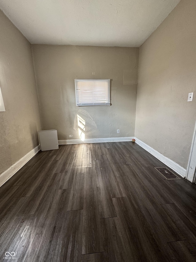 spare room with visible vents, baseboards, and dark wood-style flooring