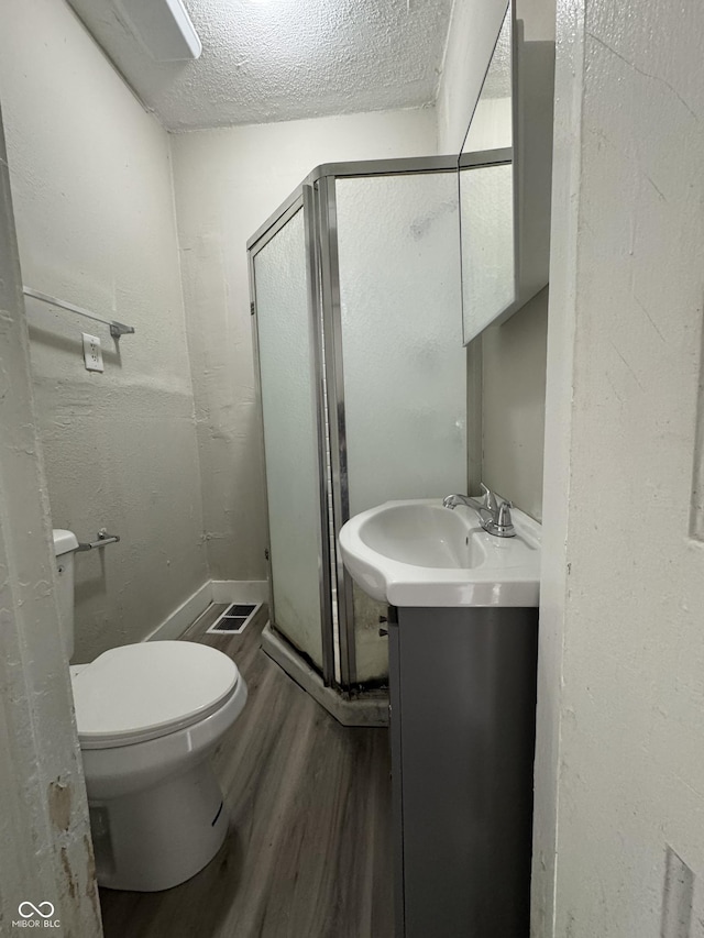 full bath featuring vanity, wood finished floors, a shower stall, a textured ceiling, and toilet