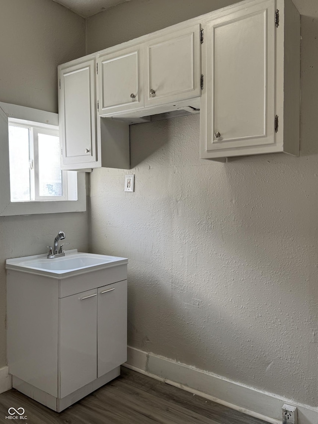 bathroom with a textured wall, vanity, baseboards, and wood finished floors