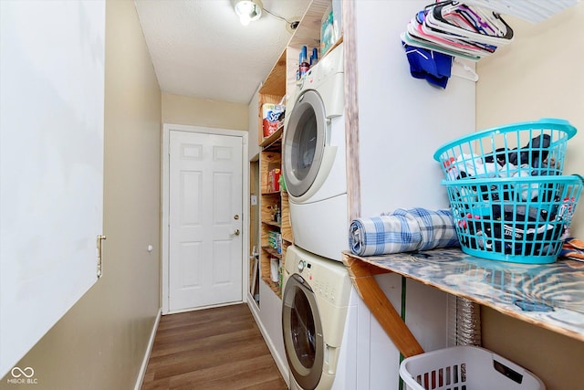 clothes washing area featuring wood finished floors, baseboards, stacked washing maching and dryer, laundry area, and a textured ceiling