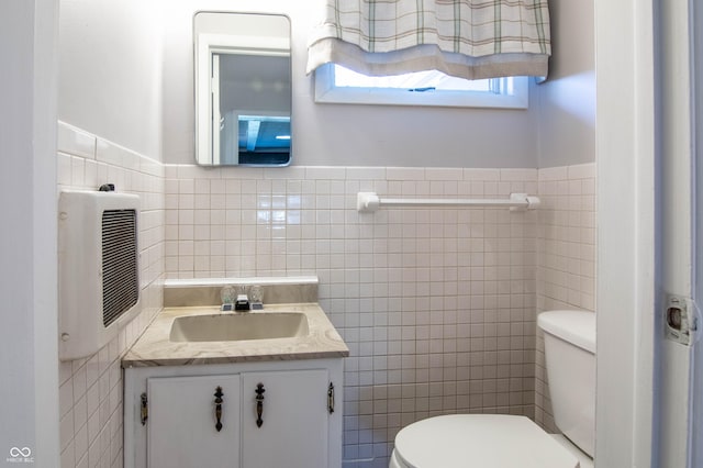 half bath with tile walls, a wainscoted wall, toilet, heating unit, and vanity