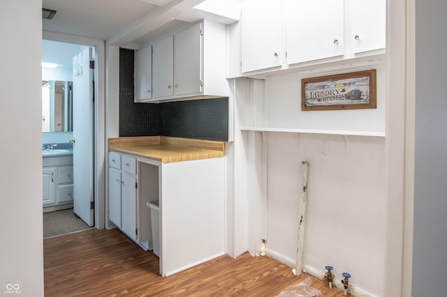 kitchen featuring light wood-style flooring, white cabinetry, light countertops, and a sink