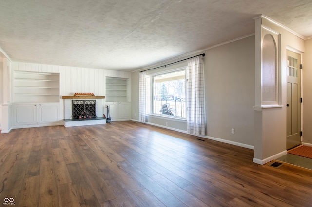 unfurnished living room featuring built in shelves, baseboards, a fireplace, a textured ceiling, and wood-type flooring