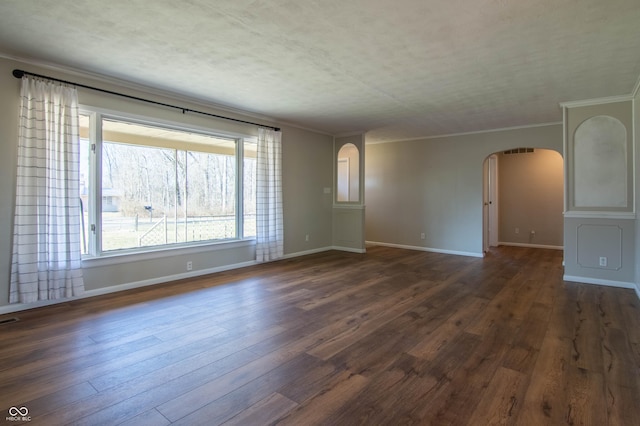 empty room featuring visible vents, crown molding, baseboards, arched walkways, and dark wood-style flooring