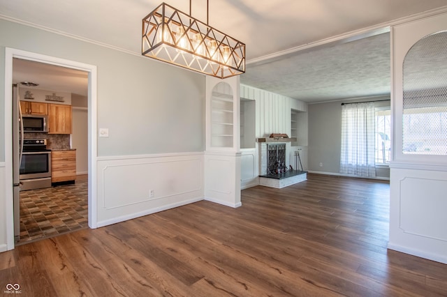 unfurnished dining area featuring dark wood-type flooring, built in features, a fireplace, wainscoting, and crown molding