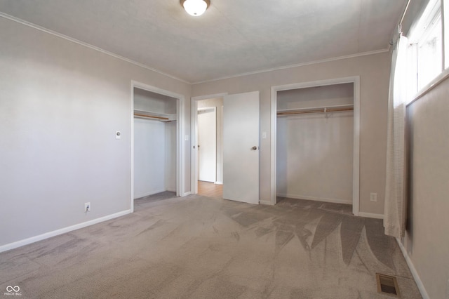 unfurnished bedroom with visible vents, two closets, baseboards, ornamental molding, and carpet flooring