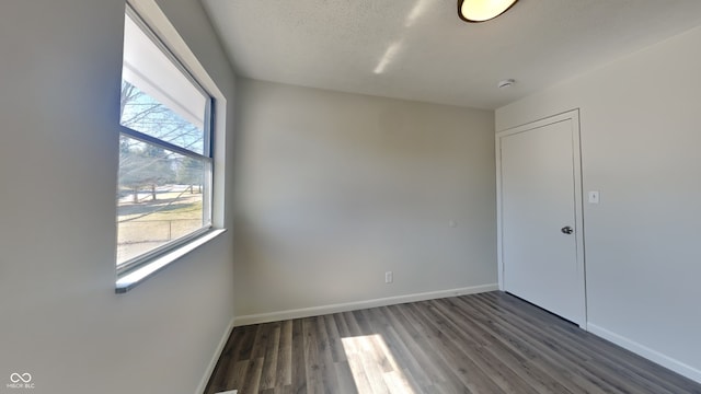 empty room with a textured ceiling, baseboards, and wood finished floors