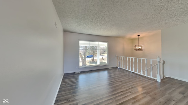 empty room with dark wood finished floors, an inviting chandelier, baseboards, and a textured ceiling