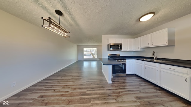 kitchen with a sink, dark countertops, wood finished floors, appliances with stainless steel finishes, and white cabinets