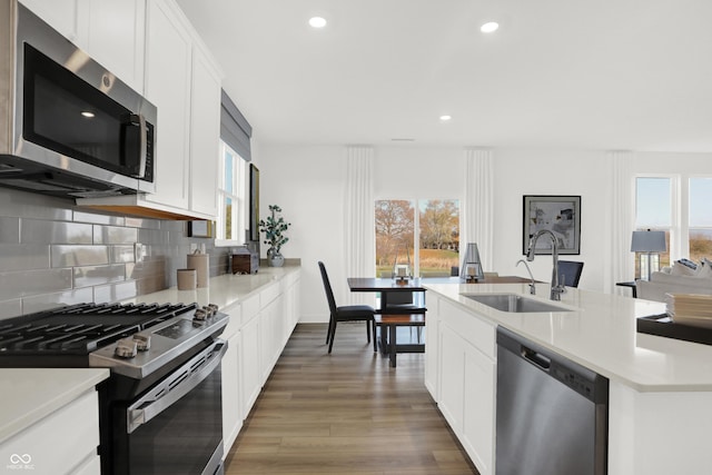 kitchen with backsplash, light countertops, appliances with stainless steel finishes, wood finished floors, and a sink