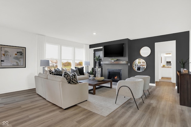 living area with baseboards, light wood-type flooring, and a warm lit fireplace