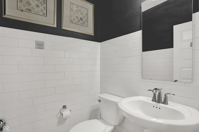 bathroom with toilet, tile walls, and a sink