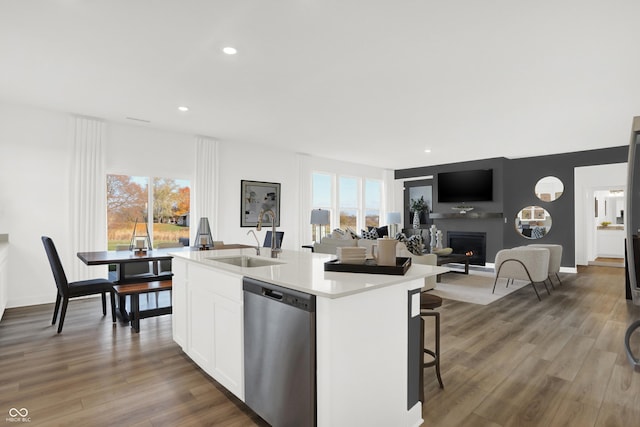 kitchen featuring wood finished floors, a center island with sink, a sink, light countertops, and stainless steel dishwasher