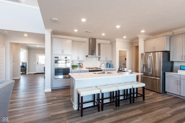 kitchen with a center island with sink, a sink, tasteful backsplash, appliances with stainless steel finishes, and wall chimney range hood