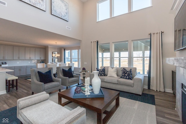 living area with visible vents, a fireplace, baseboards, a chandelier, and dark wood-style flooring