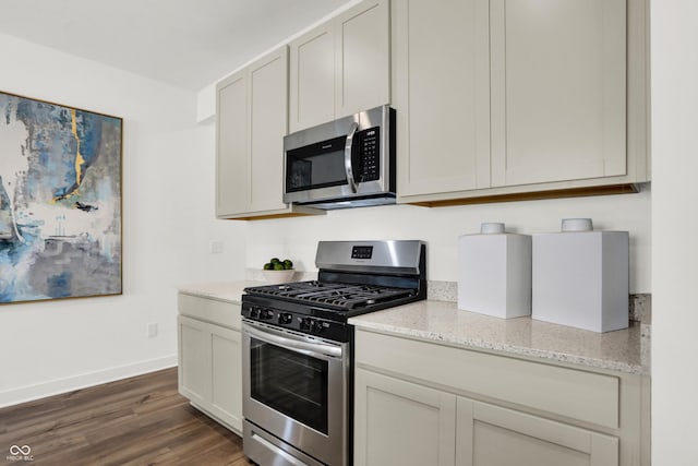 kitchen with dark wood-type flooring, light stone countertops, baseboards, and stainless steel appliances