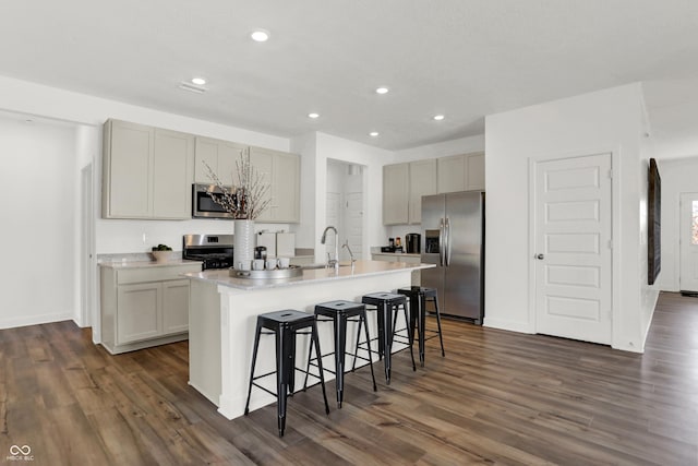 kitchen with dark wood finished floors, a center island with sink, stainless steel appliances, and a kitchen bar